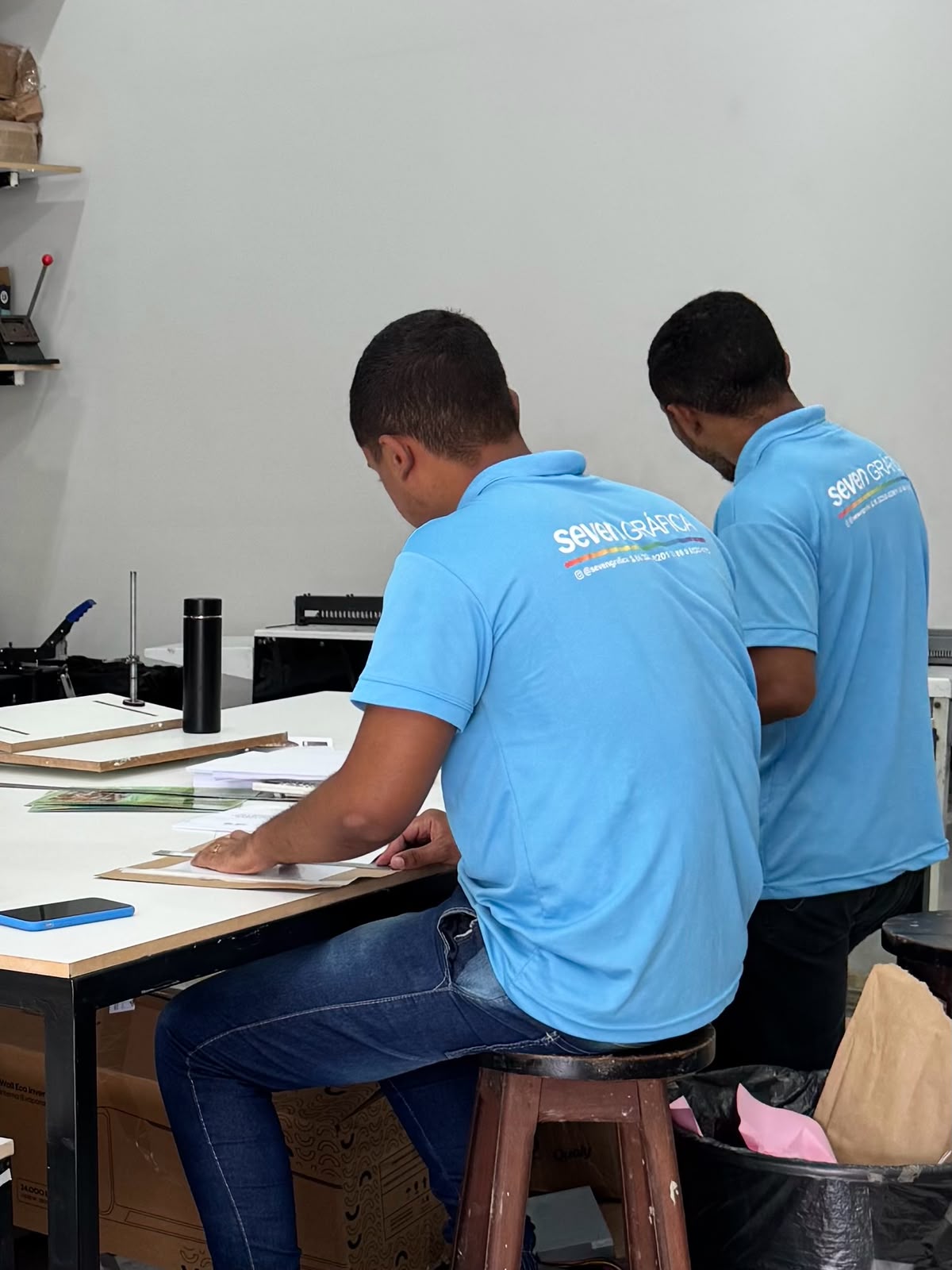 Dois colaboradores uniformizados da Seven Gráfica montando kits corporativos em bancada